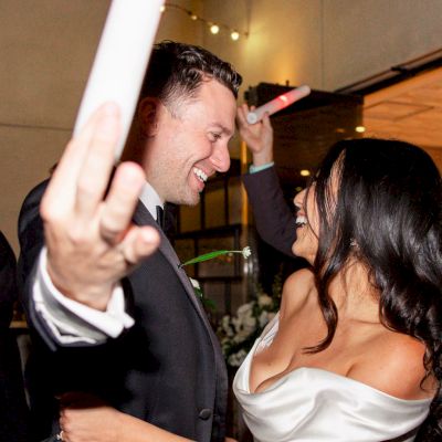 A group of people are dancing indoors, holding glowing sticks. The focus is on a couple happily interacting in the center of the scene.