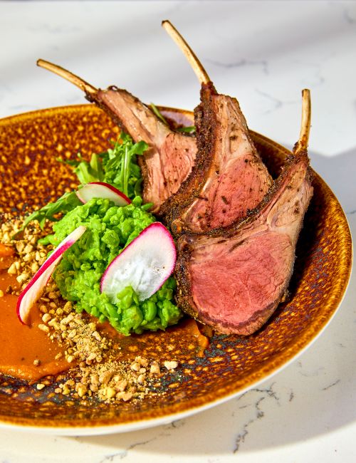 The image shows a table with bowls of salad, chicken wings, and drinks on a dark marble surface.