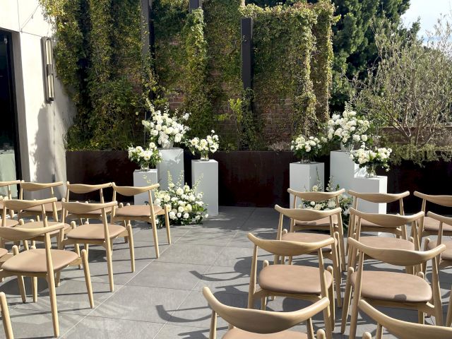 Outdoor wedding setup with arranged chairs facing a decorated floral altar, against a backdrop of greenery and clear skies.