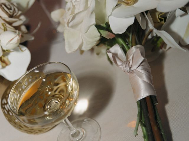 A bouquet of white flowers tied with ribbon is next to a glass of white wine on a table.