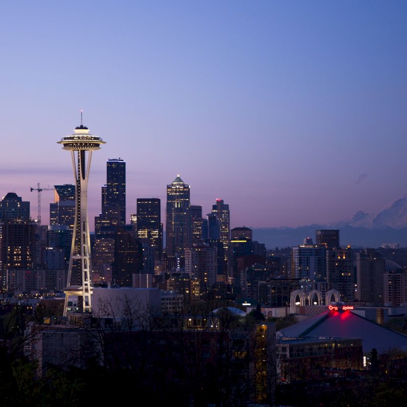 Seattle skyline at dusk with the Space Needle and Mount Rainier in the background, under a clear twilight sky.