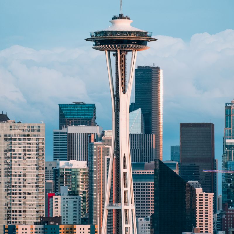 The image features the Space Needle surrounded by skyscrapers in a city skyline, with cloudy skies in the background.