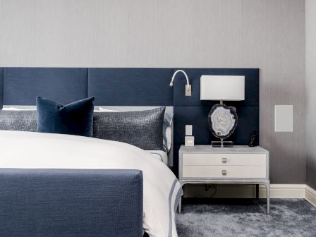 A modern bedroom with a navy and white color scheme features a bed, pillows, nightstand with lamp, and decorative accessories.
