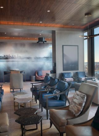 A modern lounge with comfortable seating, large windows offering a scenic view of the city and water, and a cityscape mural on the wall.