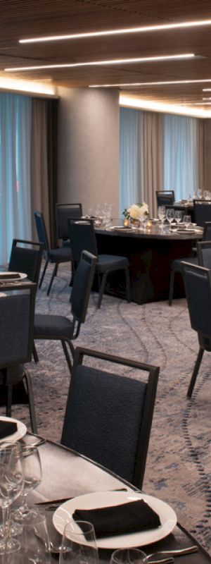 A banquet hall with round tables set for dining, featuring elegant tableware and dim lighting, ready for an event.