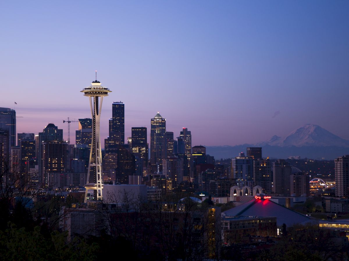 The image shows the Seattle skyline at dusk, featuring the Space Needle and Mt. Rainier in the background against a purple sunset sky.