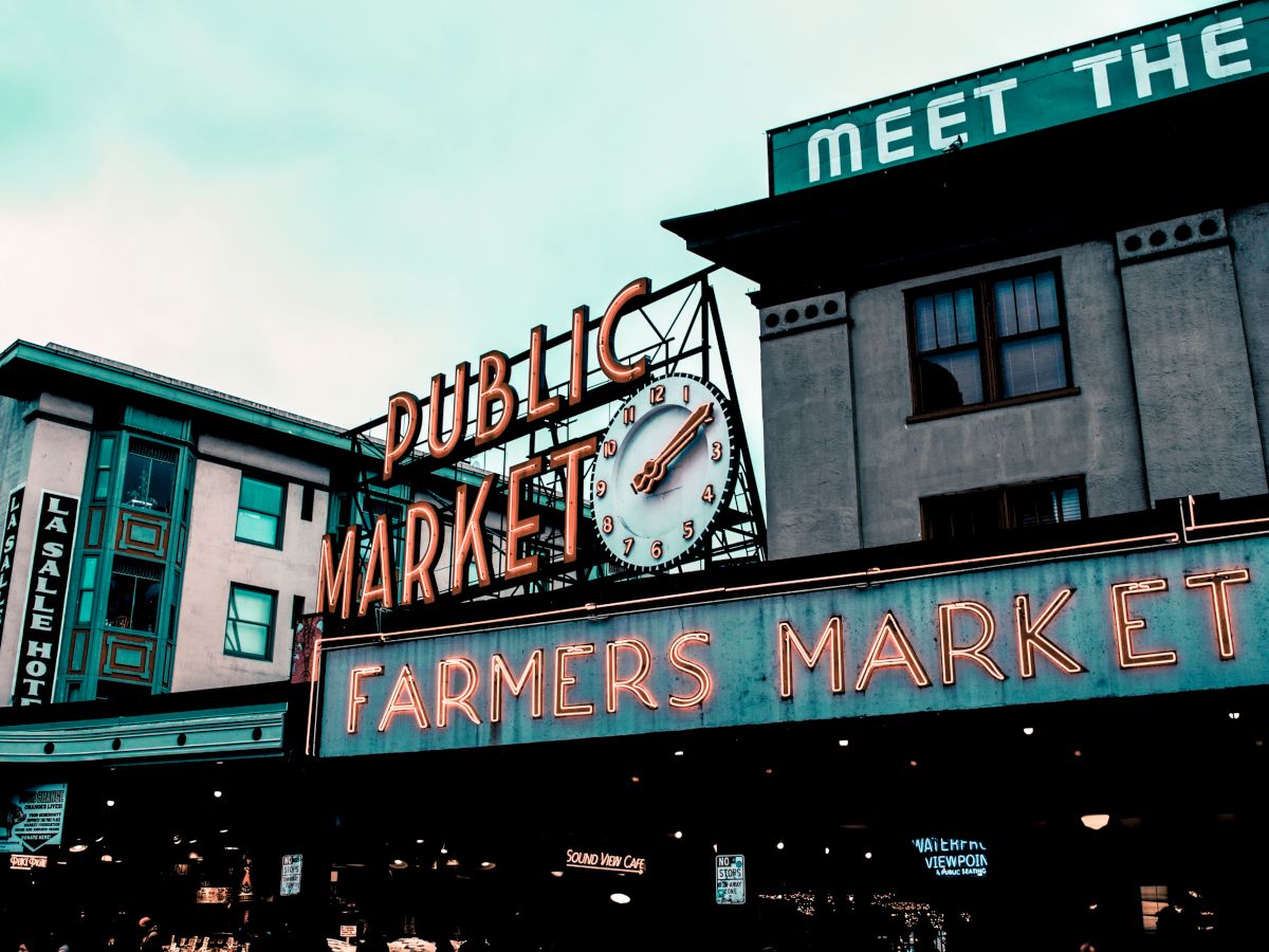 The image shows a vintage-style sign for a "Public Market" and "Farmers Market" on the exterior of a building, with a clock above.
